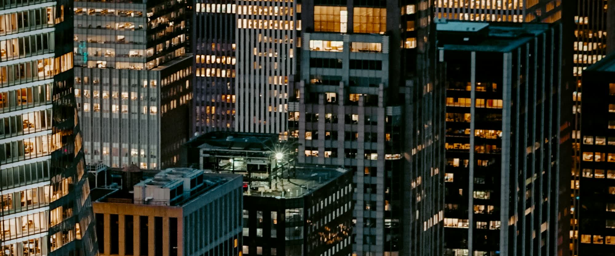 Lit office towers packed together at night, seen from above.