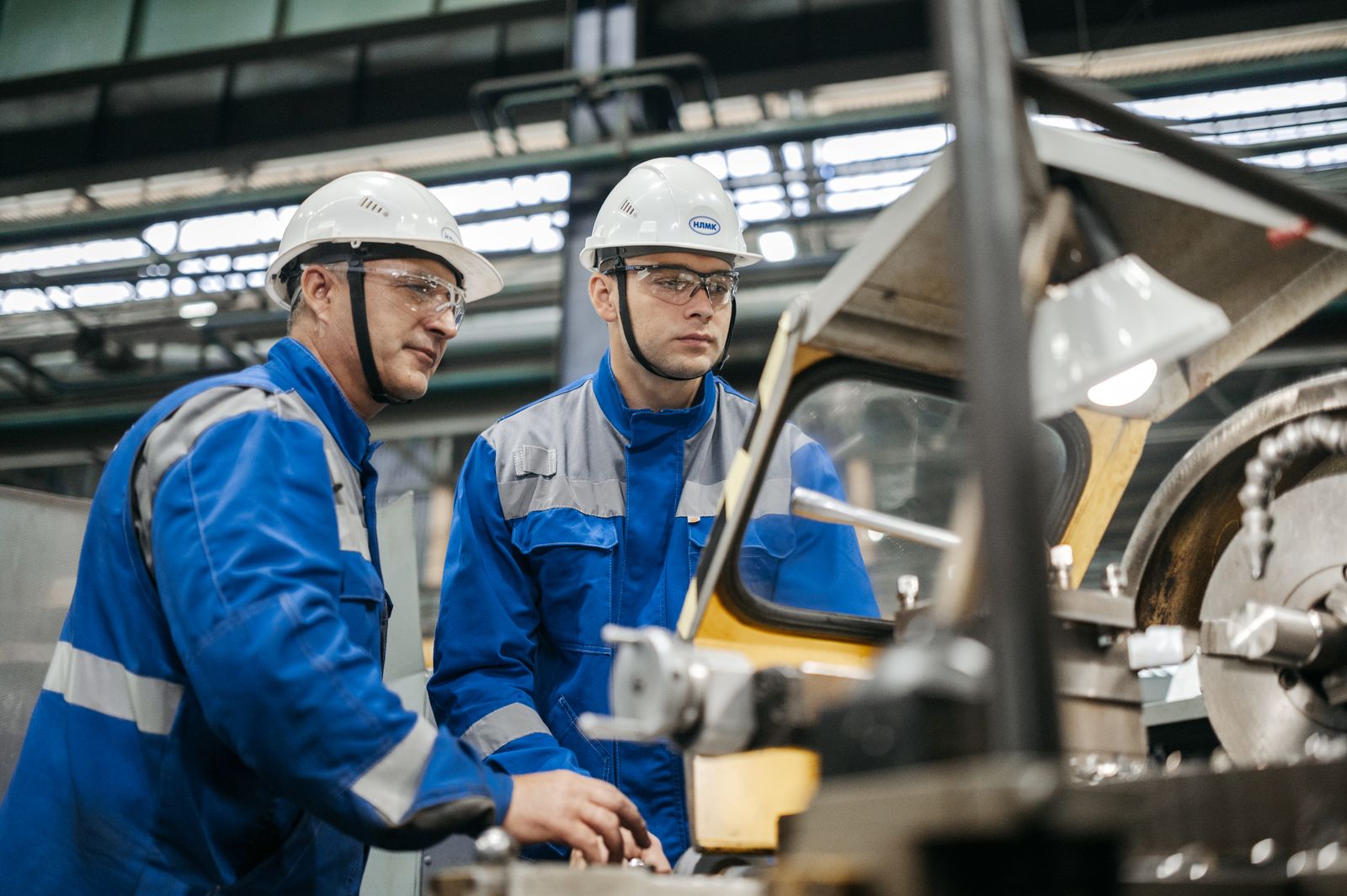 Two workers in hard hats inspecting a machine on the factory floor